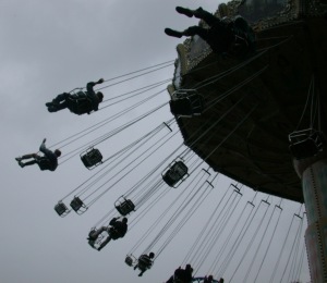 A giant machine in the air swings people strapped into harnesses centrifugally against a sky background.