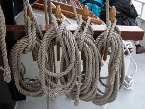 Four hanging loops of coiled rope, sensuously looped and woven, hanging on wooden hooks, maybe on a ship.