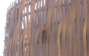 Sculptural wall of rusty bent vertical copper strips.